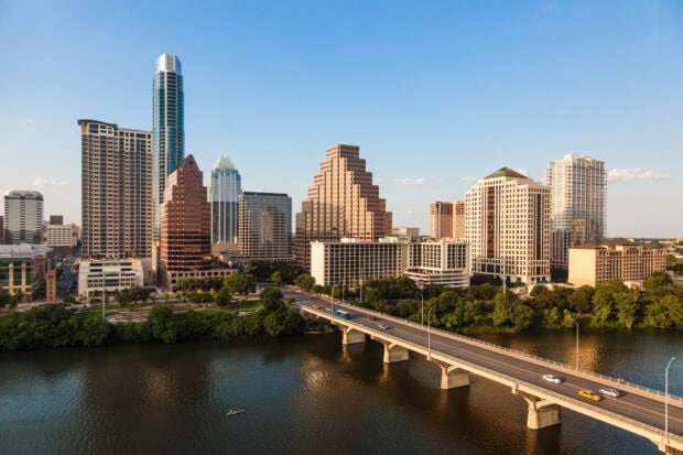 The Austin skyline features tall buildings and a bridge over the river in a clear sunny day