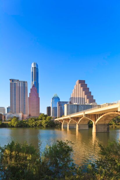 The Austin skyline is visible with buildings and a bridge over the water under a clear blue sky