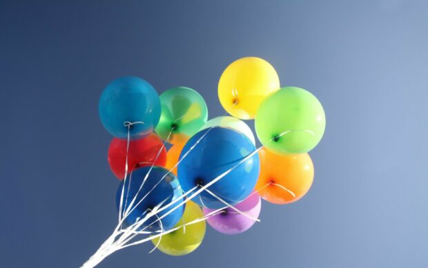 Colorful balloons floating in the clear sky with bright vibrant colors and strings attached