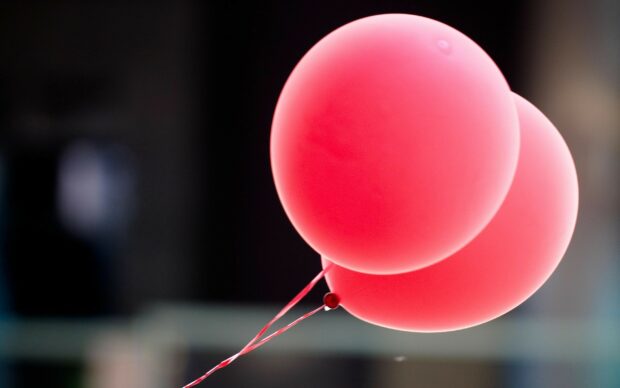 Two red balloons floating with strings against a blurred dark background