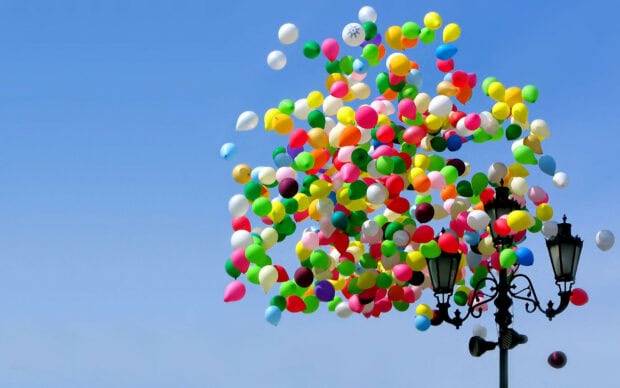 A large cluster of colorful balloons floating in the clear blue sky above a street lamp