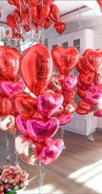 A bunch of heart shaped balloons in red pink and gold colors floating in a modern room