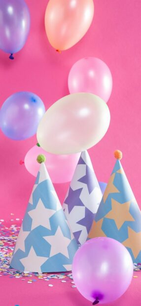 Colorful balloons floating over party hats on a pink background