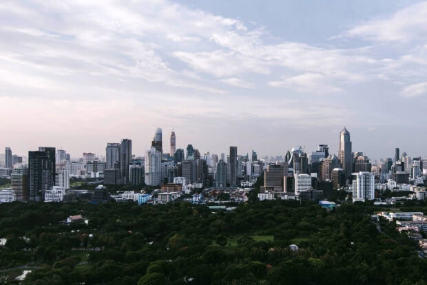 A panoramic view of Bangkok skyline with numerous skyscrapers and lush green park in the foreground