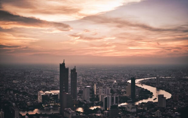 Bangkok skyline with tall buildings along a river at sunset in the cityscape
