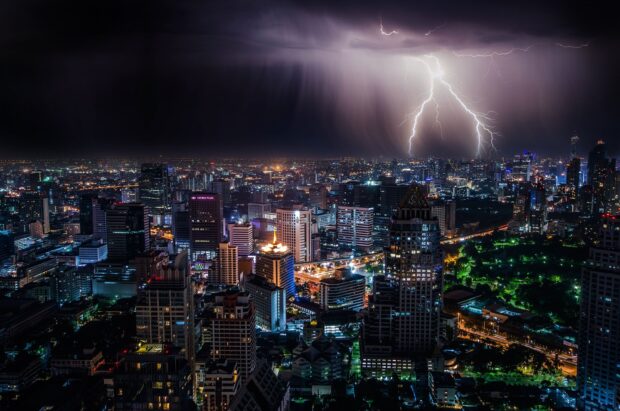 Lightning striking over Bangkok skyline at night with city lights and storm clouds