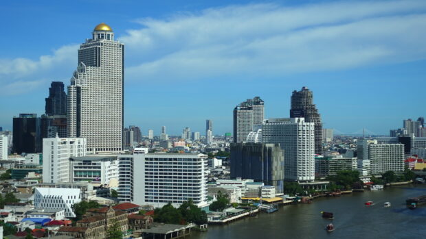 A clear view of Bangkok skyline featuring tall buildings and a river under blue sky