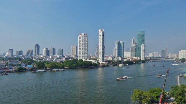 A panoramic view of the Bangkok skyline featuring tall buildings along the river in clear weather