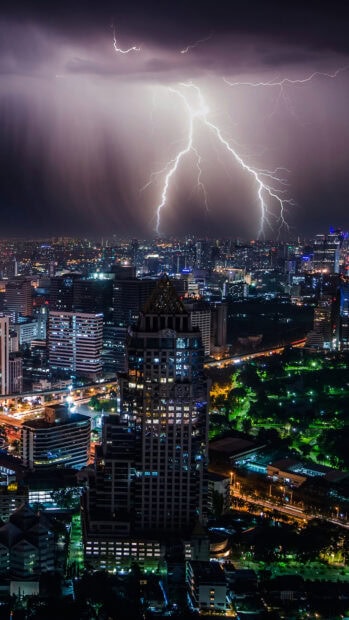 Thunderstorm over Bangkok skyline with lightning striking during night in cityscape
