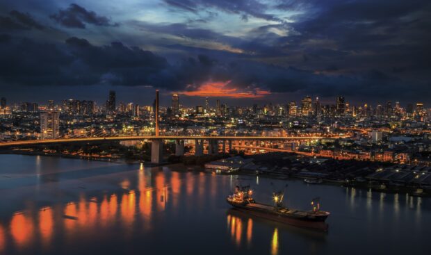 Night view of Bangkok city skyline with river and lit bridge reflecting lights in the water