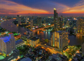 Cityscape of Bangkok at sunset with river and illuminated buildings in vibrant colors