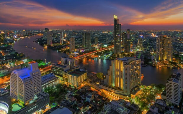 Cityscape of Bangkok at sunset with river and illuminated buildings in vibrant colors