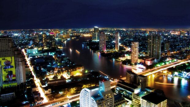 Night cityscape of Bangkok with illuminated buildings and river lights reflecting on the water