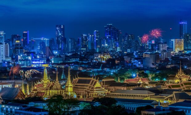 Night view of Bangkok cityscape with fireworks and golden temples illuminated in the foreground