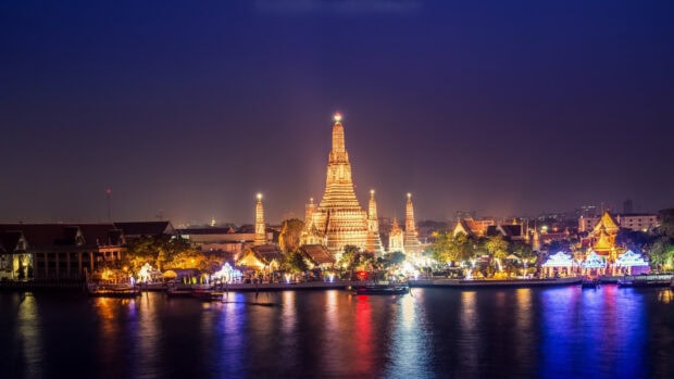 Night view of Bangkok temple illuminated along the river reflecting colorful lights