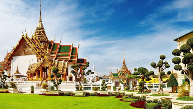 Traditional Bangkok architecture with golden roofs and manicured trees under a blue sky