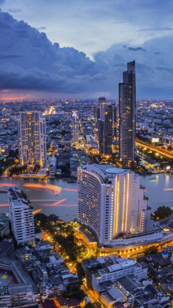 Evening cityscape of Bangkok showing illuminated buildings and river lights at sunset