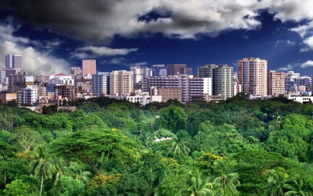 Lush Bangladesh cityscape with green trees and tall buildings under dramatic clouds