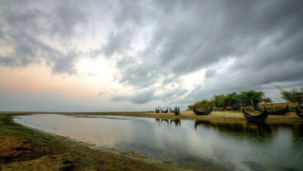 Traditional Bangladesh boats lined up along a riverbank under a cloudy sky