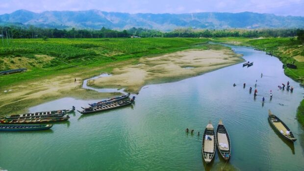 A peaceful river in Bangladesh with traditional wooden boats and lush green fields