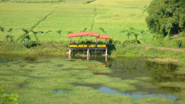 A scenic view of Bangladesh last house over green fields and water in rural area