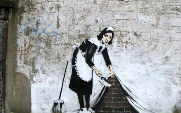 A Banksy street art stencil of a maid lifting a wall to reveal bricks underneath