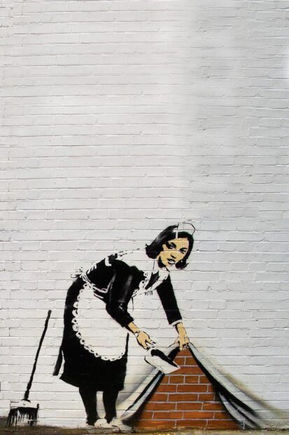 A Banksy artwork showing a maid sweeping dirt under a brick wall panel
