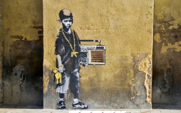 Banksy graffiti of a boy holding a teddy bear and boombox on a textured wall