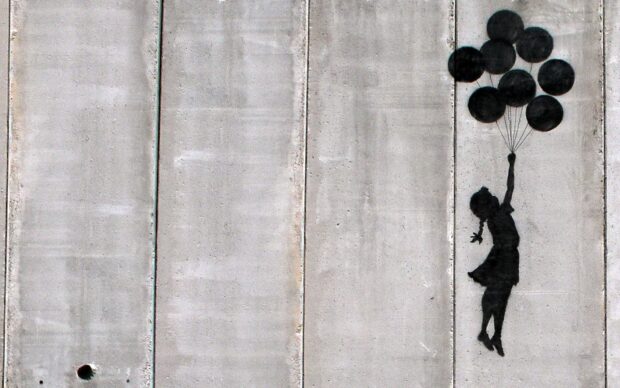 Banksy street art stencil of a girl holding balloons floating on a concrete wall