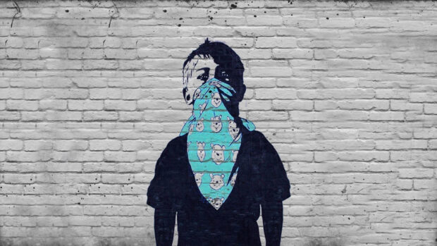 Street art of a person wearing a blue scarf with cartoon faces on a brick wall