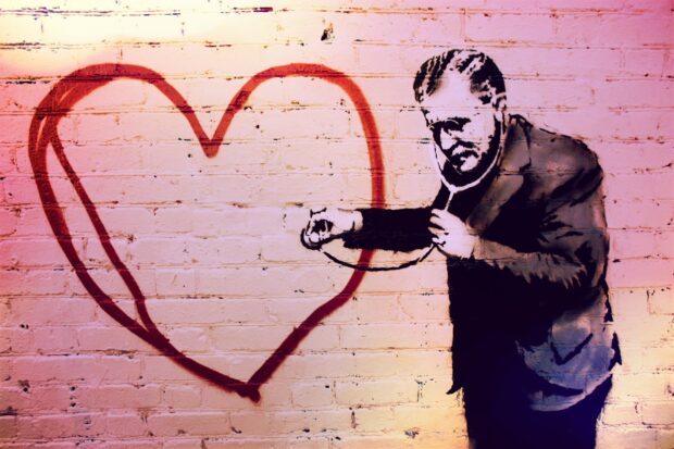 A Banksy graffiti artwork showing a man with a stethoscope examining a red heart painted on a brick wall