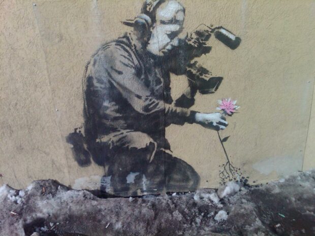 A Banksy mural shows a person holding a flower with a camera on their shoulder