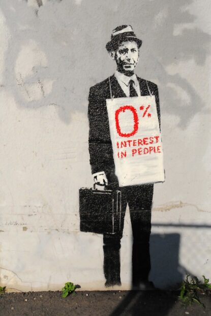 A Banksy stencil art of a man in a suit holding a briefcase with a sign showing zero percent interest in people
