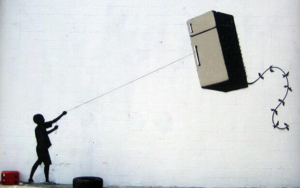 A Banksy street art showing a child flying a refrigerator like a kite on a white wall