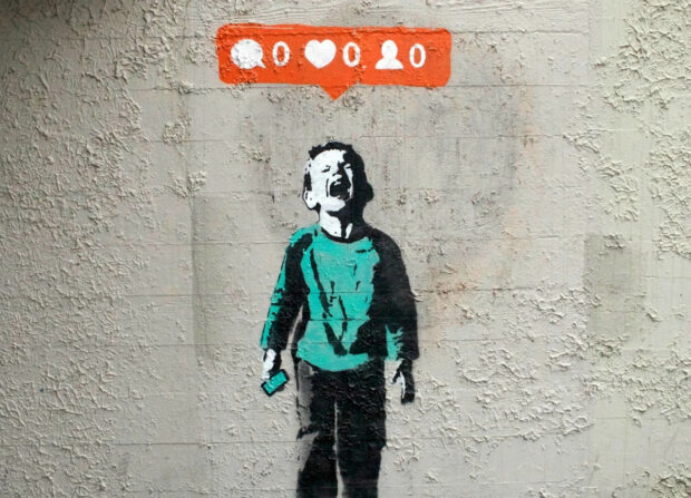 Banksy art depicts a boy crying under a social media notification symbol on a textured wall