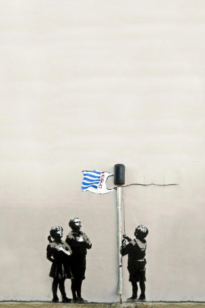 Three children stand solemnly with one hoisting a Tesco flag on a pole