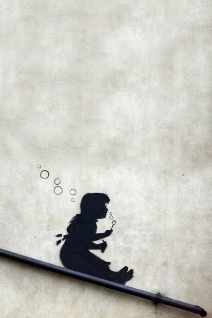 A Banksy graffiti of a child sitting and blowing bubbles on a wall near a pipe