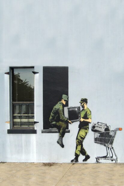 Soldiers transferring a television in street art by Banksy on a white wall