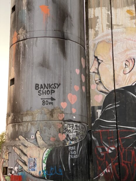 Street art graffiti featuring Banksy shop sign and a man with pink hearts on a concrete wall
