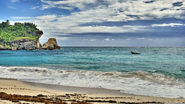 A scenic view of Barbados coastline with lush greenery and a boat on the turquoise sea