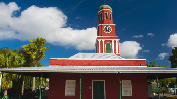 Historic clock tower in Barbados under a bright blue sky with palm trees nearby