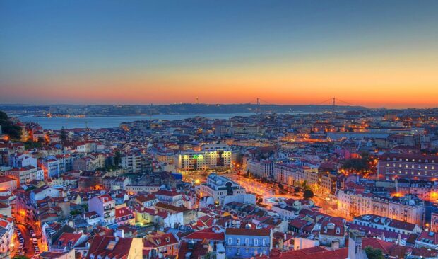 A panoramic view of Barcelona city during sunset with lit buildings and a distant bridge