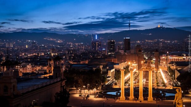 Night view of Barcelona cityscape with illuminated pillars and buildings at dusk