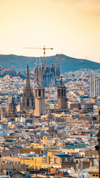 Barcelona cityscape featuring historical towers with cranes and mountains in the background