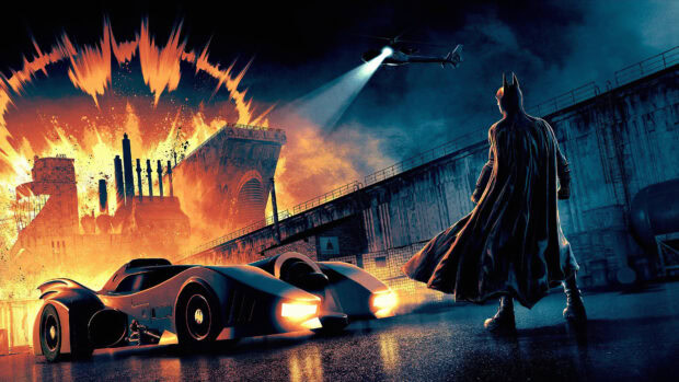 Batman stands near the Batmobile with an industrial explosion in the background