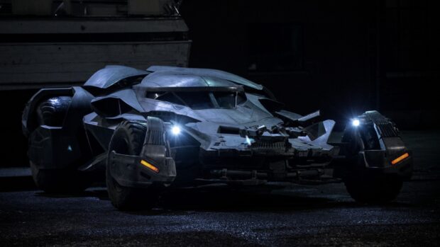 Dark armored Batmobile with glowing headlights on a wet surface at night