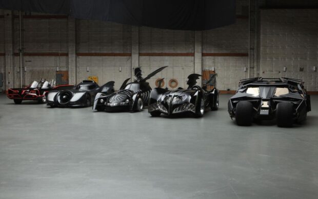 A lineup of iconic Batmobile models showcasing various designs in a spacious garage setting