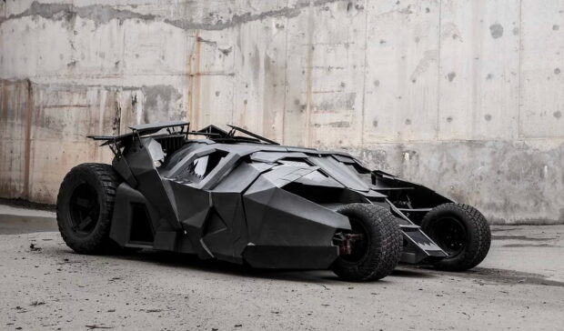 A sleek Batmobile parked against a concrete wall in an industrial setting