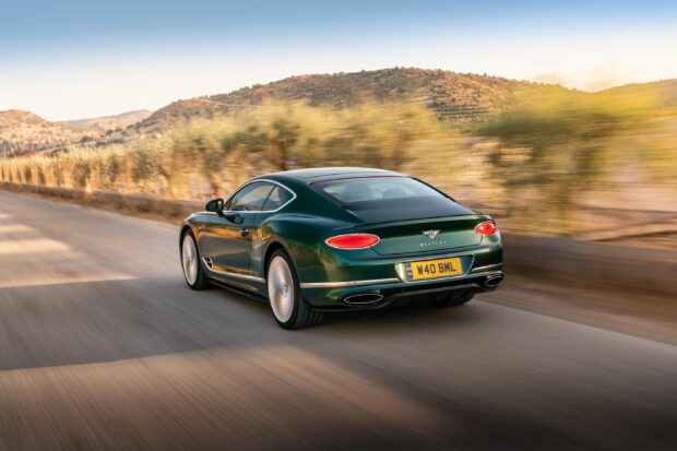 A green Bentley Continental driving fast on a countryside road with hills in the background