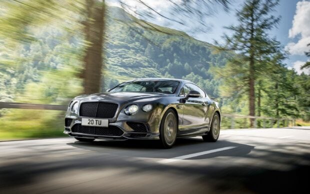A Bentley Continental luxury car driving fast on a forest road with mountains in the background